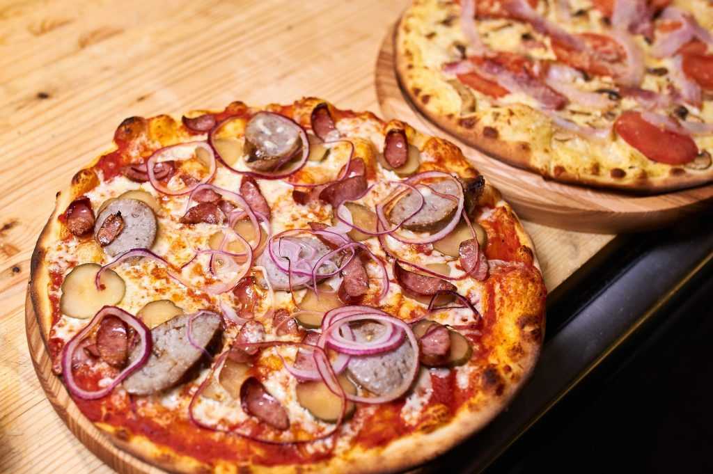 Two Freshly baked pizza with bacon, onion and pepper lie on a wooden table.